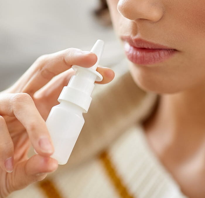 A person holds a white nasal spray bottle close to their nose, preparing to use it.