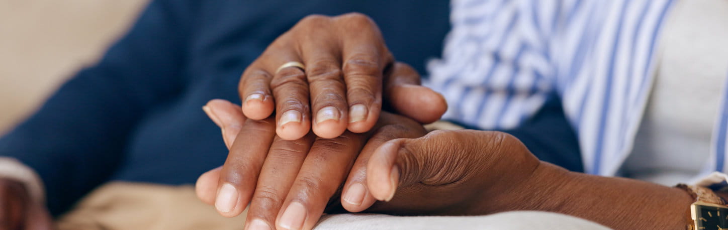 Close-up of two people holding hands, one hand gently resting on top of the other, suggesting comfort and support.
