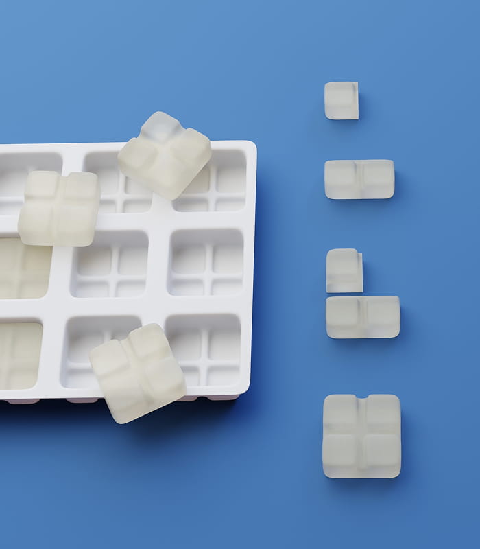 A white ice cube tray with several ice cubes, some in the tray and others arranged in lines on a blue surface.