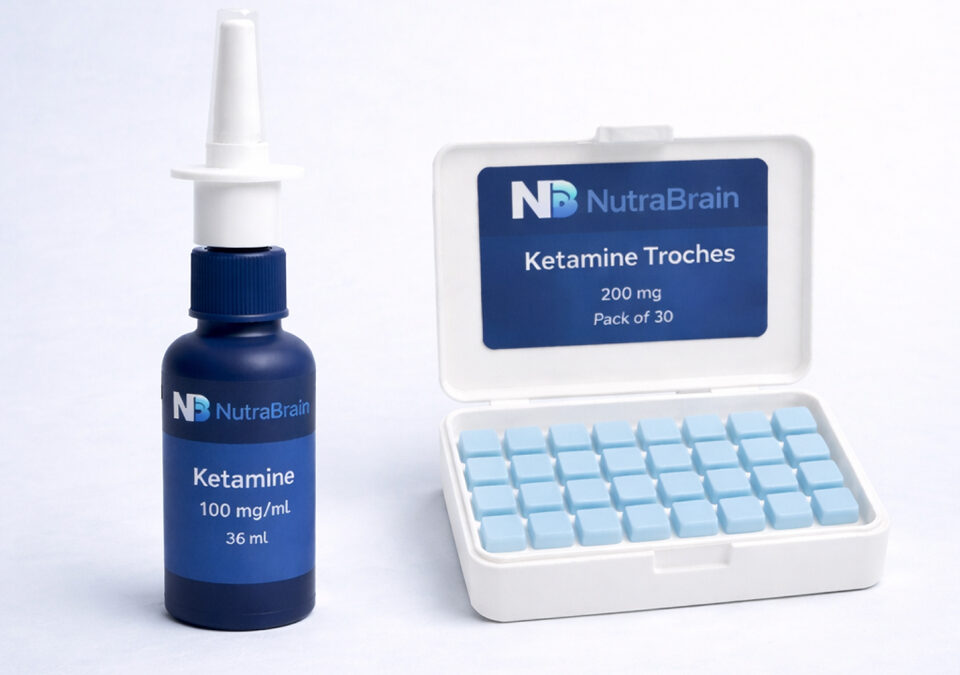 A bottle labeled "Ketamine 100 mg/mL" with a nasal spray top is next to an open case of "Ketamine Troches 200 mg," containing 30 light blue tablets.