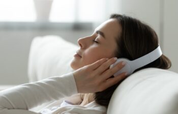 Calm female resting leaned on comfy couch in living room spend free time at home closed eyes enjoy music listening favourite song through wireless modern headphones. Pastime weekend relaxation concept