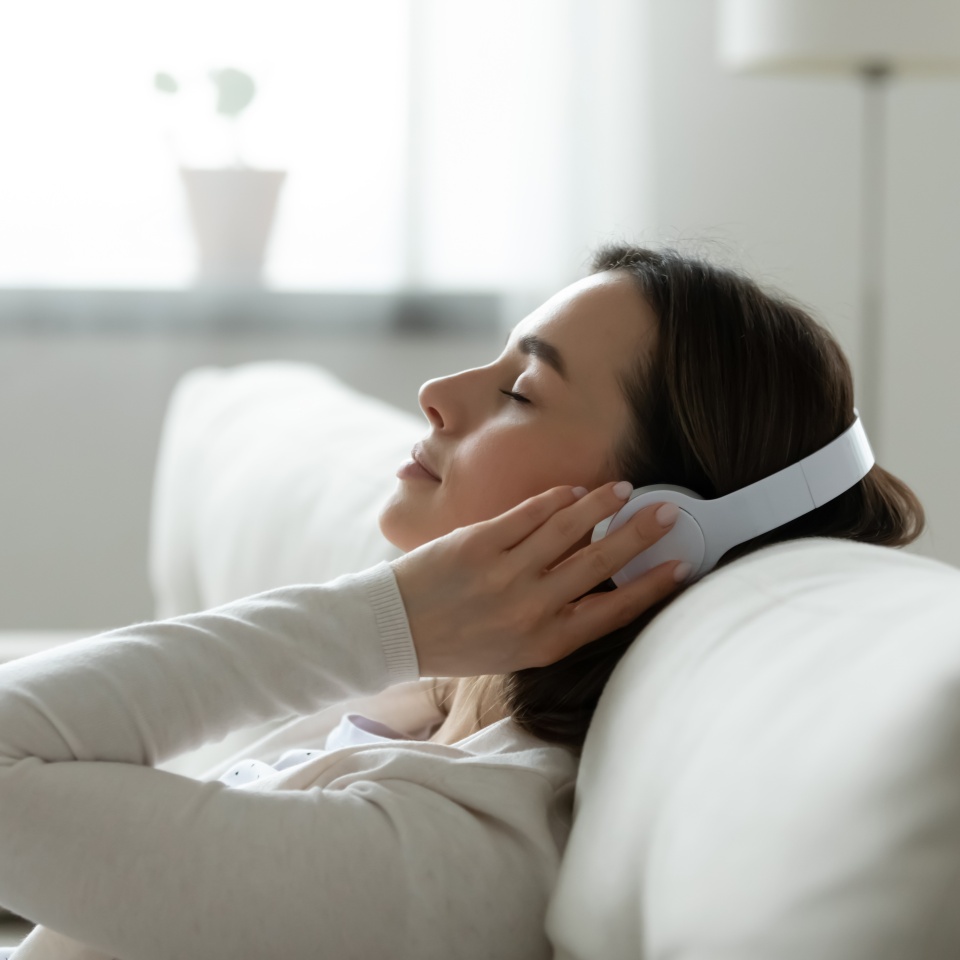 Calm female resting leaned on comfy couch in living room spend free time at home closed eyes enjoy music listening favourite song through wireless modern headphones. Pastime weekend relaxation concept