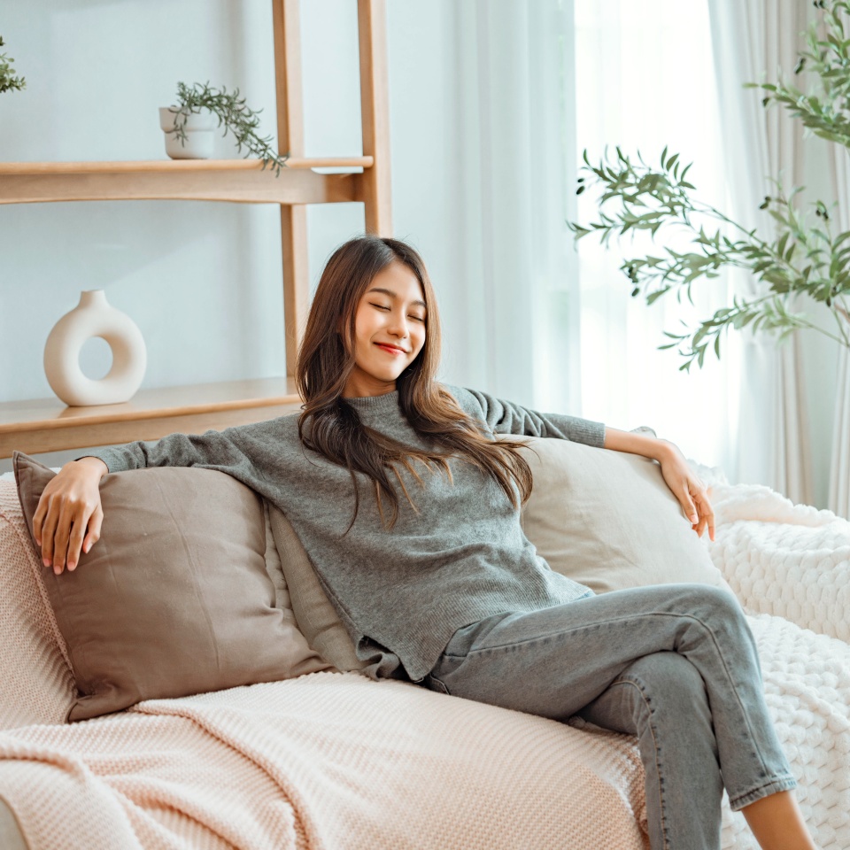 Relaxed young asian woman enjoying rest on comfortable sofa at home, calm attractive girl relaxing and breathing fresh air in home.