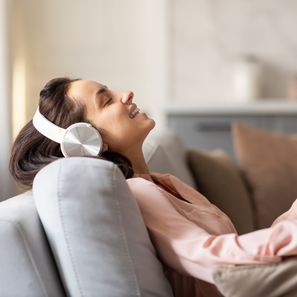 Contented woman with closed eyes savoring the moment, relaxing on sofa with stylish headphones, deeply immersed in her music-filled respite