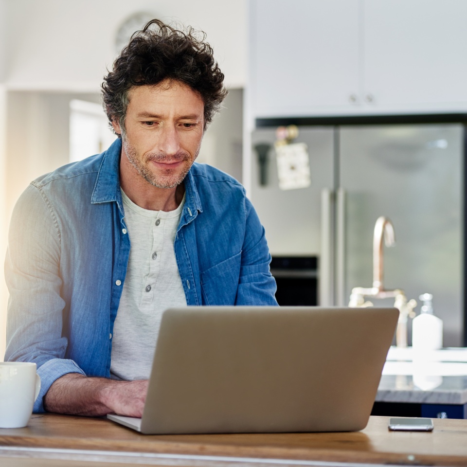 Man, laptop or typing in kitchen for remote work, web designer with check for schedule. Male entrepreneur, computer or reading in home for creative development, digital administration with technology