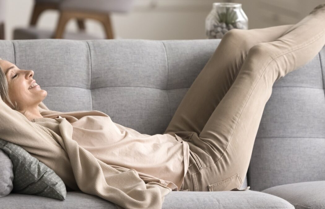 Peace of mind. Smiling tranquil mid aged woman take time to relax on comfy couch give tired legs a rest after hard work day enjoy calm serene house space listen to quiet music dream with closed eyes