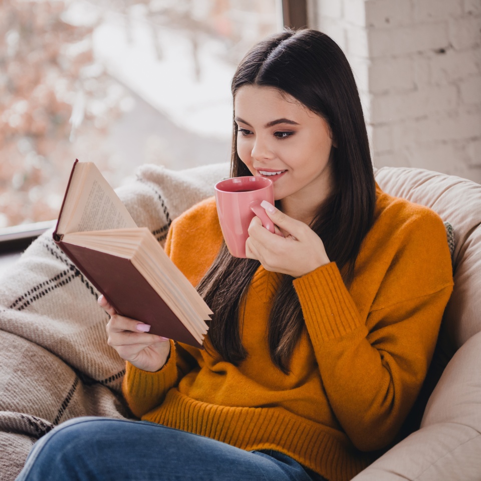 Young woman enjoying a relaxing day at home with a book and coffee in a cozy indoor setting