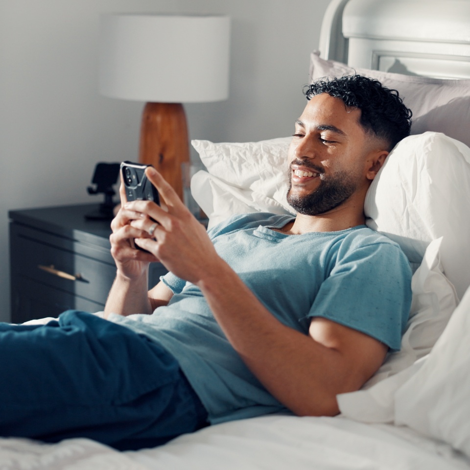 Man, phone and relax in bedroom for communication, social media or reading ebook on weekend at home. Male person, mobile app with text message or blog, email and contact with connectivity on day off