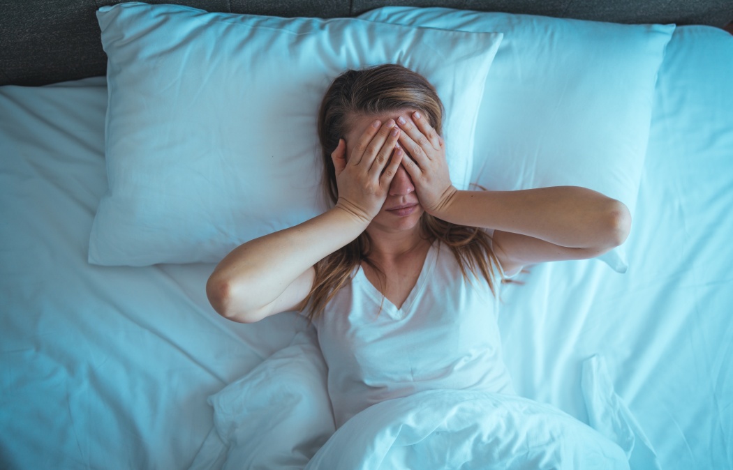 Young stressed woman lying on bed late at night suffering from insomnia, sleep apnea or stress. Top view of depressed girl lying bed. High angle view of awake girl in the middle of the night.