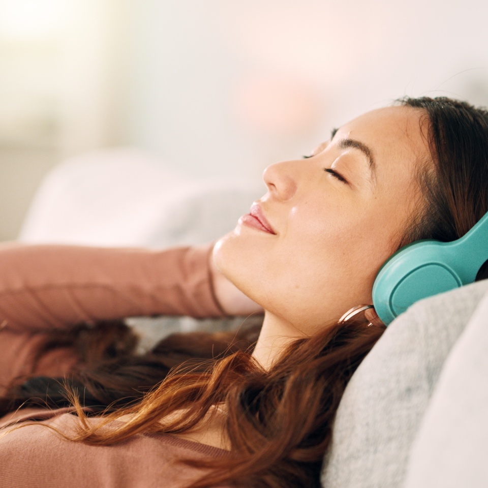 Woman headphones, listening to relax music, podcast and smile with a calm, zen and peaceful day at home. Happy Asian female and relaxed woman sitting on a living room sofa and meditation with audio