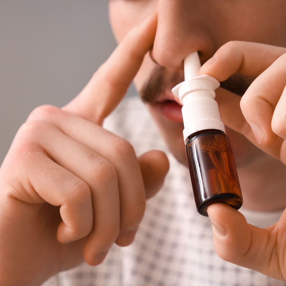 Ill young man using nasal drops at home, closeup